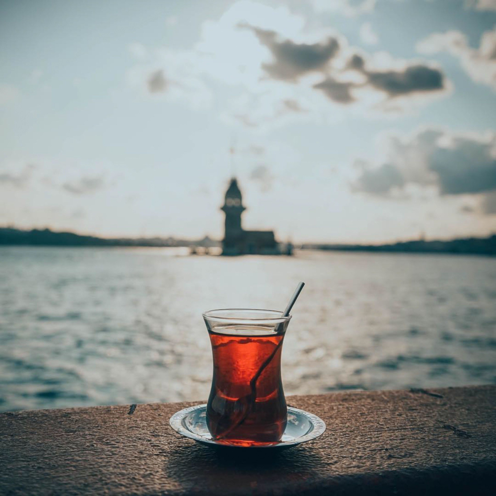 Glas mit schwarzem Tee vor einer ruhigen Wasserlandschaft